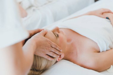 Lüks kaplıcalarda spa masajı ve rahatlama için yatakta uzanan güzel bir kadın. Masör yüzüne ve kafasına spa odasında masaj yaptı..