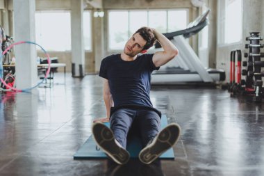 Spor salonunda yoga minderleri üzerinde egzersiz yapmadan önce esneme hareketleri yapan atletik erkekler. Boyun kaslarını esneterek..
