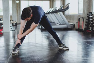 Spor salonunda yoga minderleri üzerinde egzersiz yapmadan önce esneme hareketleri yapan atletik erkekler. Bacak kaslarını esneterek..