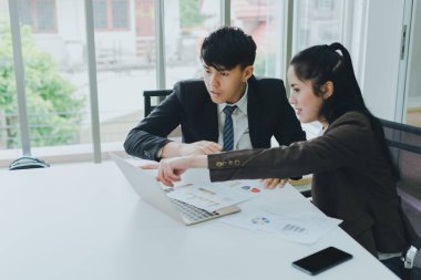 Asyalı erkek ve bayan meslektaşlar grafik kağıdı ve bir not defteri üzerinde çalışıyorlar..