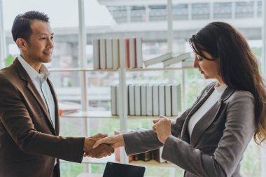 Asyalı iş adamları genç iş adamlarıyla iş anlaşmaları yapabilir. Bu yüzden her ikisi de bir iş anlaşmasını başardıkları için tebrik etmek için el ele tutuşuyor..