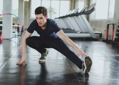 Spor salonunda yoga minderleri üzerinde egzersiz yapmadan önce esneme hareketleri yapan atletik erkekler. Bacak kaslarını esneterek..