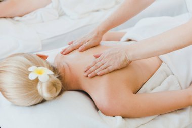 Lüks kaplıcalarda spa masajı ve rahatlama için yatakta uzanan güzel bir kadın. Masöz, masaj odasında sırtına ve omuzlarına masaj yapıyor..