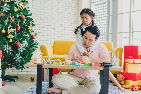 Asian father and daughter play toys on the table in the living room decorated with Christmas trees to prepare for Christmas and New Year\'s celebrations.