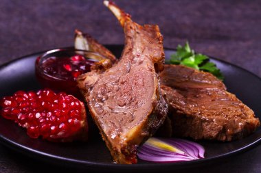 Karanlık dokusal arka plan üzerinde siyah plaka nar soslu kuzu ızgara raf