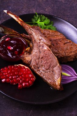 Karanlık dokusal arka plan üzerinde siyah plaka nar soslu kuzu ızgara raf