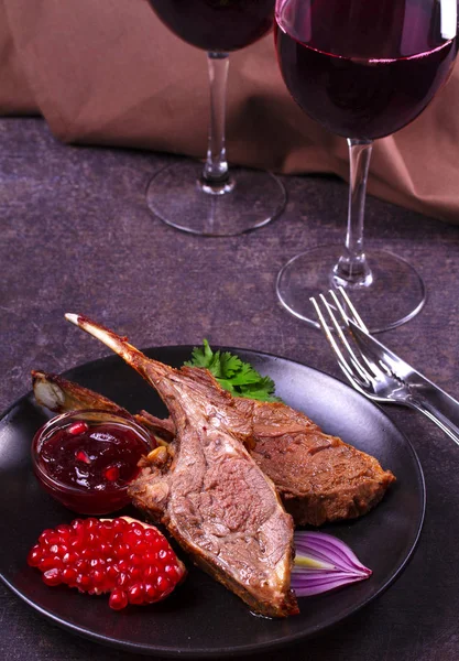 Grilled rack of lamb with pomegranate sauce in black plate on dark textural background — Stock Photo, Image