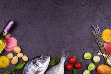 Brüksel lahanası, domates, limon, genç patates, yeşillik, ekmek, beyaz şarap şişesi ve zeytinyağı koyu arka plan üzerinde ham dorado balık