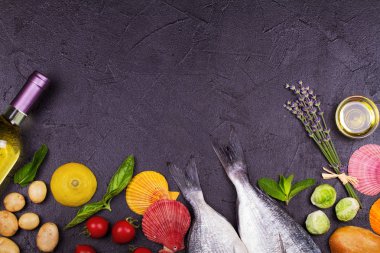 Brüksel lahanası, domates, limon, genç patates, yeşillik, ekmek, beyaz şarap şişesi ve zeytinyağı koyu arka plan üzerinde ham dorado balık