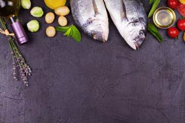 Brüksel lahanası, domates, limon, genç patates, yeşillik, ekmek, beyaz şarap şişesi ve zeytinyağı koyu arka plan üzerinde ham dorado balık