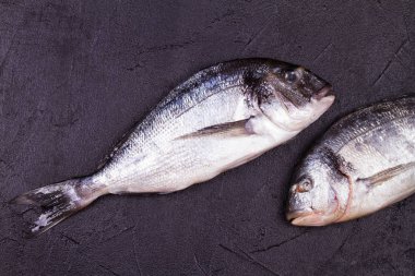 Brüksel lahanası, domates, limon, genç patates, yeşillik, ekmek, beyaz şarap şişesi ve zeytinyağı koyu arka plan üzerinde ham dorado balık