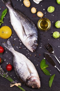 Brüksel lahanası, domates, limon, genç patates, yeşillik, ekmek, beyaz şarap şişesi ve zeytinyağı koyu arka plan üzerinde ham dorado balık