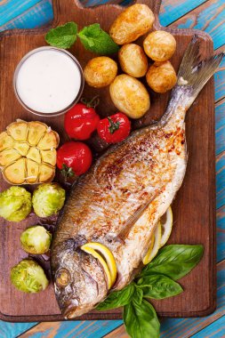 Brüksel lahanası, domates, sarımsak, genç patates ve Yeşiller kesme tahtası üzerinde broiled dorado balık