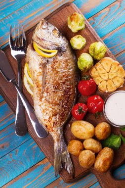Brüksel lahanası, domates, sarımsak, genç patates ve Yeşiller kesme tahtası üzerinde broiled dorado balık