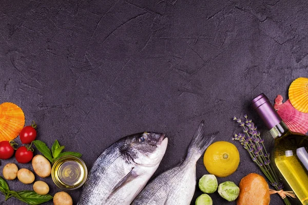 Raw fresh dorado fish with brussels sprouts, tomatoes, lemon, young potato, greens, bread, white wine bottle and olive oil on dark background — Stock Photo, Image