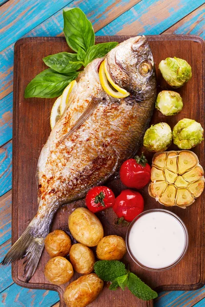 Pieczonej ryby dorado z brukselka, pomidory, czosnek, młodych ziemniaków i zieleni na deska do krojenia — Zdjęcie stockowe