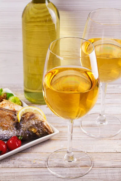 Очки и бутылка белого вина. Жареная рыба с овощами в белой тарелке — стоковое фото