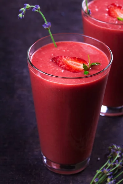 Berry smoothie garnerad med jordgubbar och lavendelblommor på mörk trä bakgrund — Stockfoto