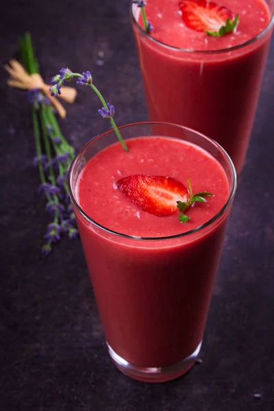 Berry smoothie adornado con fresas y flores de lavanda sobre fondo de madera oscura — Foto de Stock