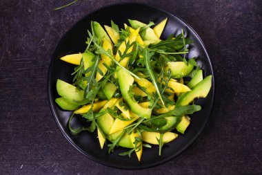 Siyah plaka üzerinde avokado, mango ve Roka Salatası