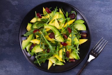 Avokado, mango, kırmızı üzüm ve Roka Salatası siyah plaka üzerinde