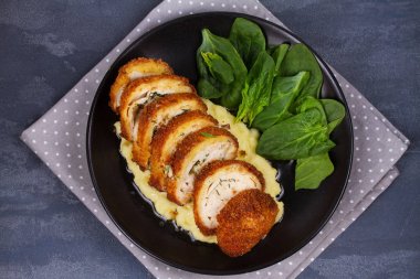 Tavuk Kiev ıspanaklı patates püresi üzerinde. Otlar ve siyah plaka üzerine tereyağı ekmekli tavuk göğsü dolması