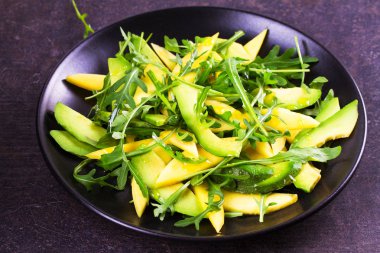 Avokado, mango, kırmızı üzüm ve Roka Salatası siyah plaka üzerinde