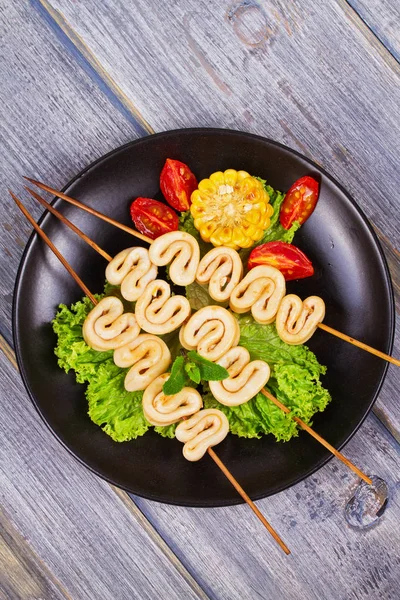 Жареные кольца кальмара на шампуре и овощи на черной тарелке — стоковое фото
