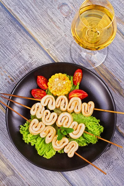 Жареные кольца кальмара на шампуре и овощи на черной тарелке — стоковое фото