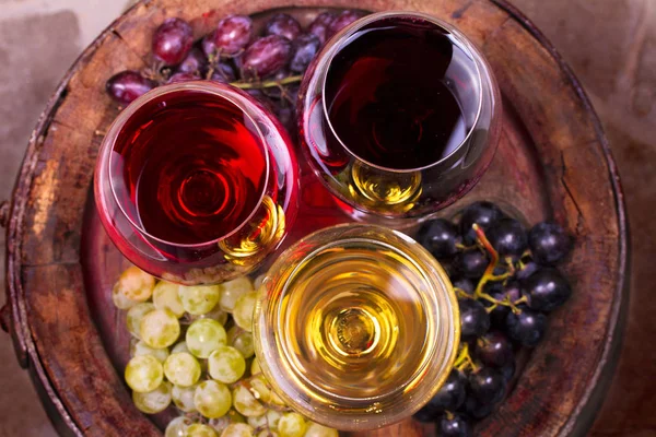 Gläser Rot-, Rosen- und Weißwein mit Trauben im Weinkeller. Konzept für Speisen und Getränke — Stockfoto