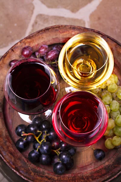 Glasses of red, rose and white wine with grape in wine cellar.  Food and drinks concept