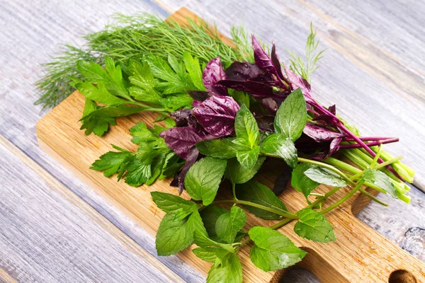 Kruiden op houten snijplank: Dille, peterselie, munt en basilicum. Culinaire kruiden voor het koken en eten bijgerechten — Stockfoto