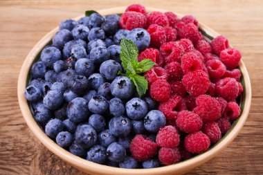 Yaban mersini ve ahududu kil kase. Taze çilek rustik arka plan üzerinde aldı