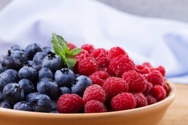 Yaban mersini ve ahududu kil kase. Taze çilek rustik arka plan üzerinde aldı