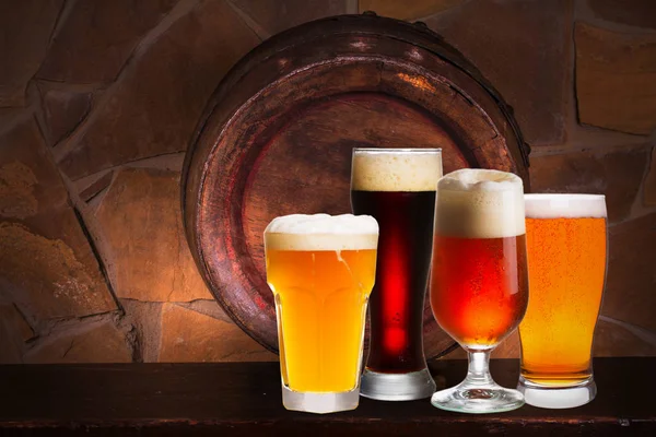 Set of various glasses of beer in cellar, pub or restaurant. Beer glasses, old beer barrel and brick wall on background