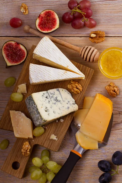 Cheese plate. Various types of cheese with grapes, honey, figs and nuts on rustic wooden table — Stock Photo, Image