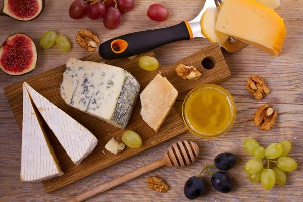 Cheese plate. Various types of cheese with grapes, honey, figs and nuts on rustic wooden table — Stock Photo, Image