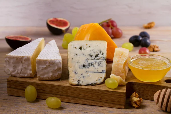 Cheese plate. Various types of cheese with grapes, honey, figs and nuts on rustic wooden table — Stock Photo, Image