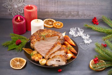 Çatal, bıçak ve rustik koyu arka plan üzerinde şenlikli dekorasyon ile dilimlenmiş Noel jambonu plaka üzerinde kavrulmuş