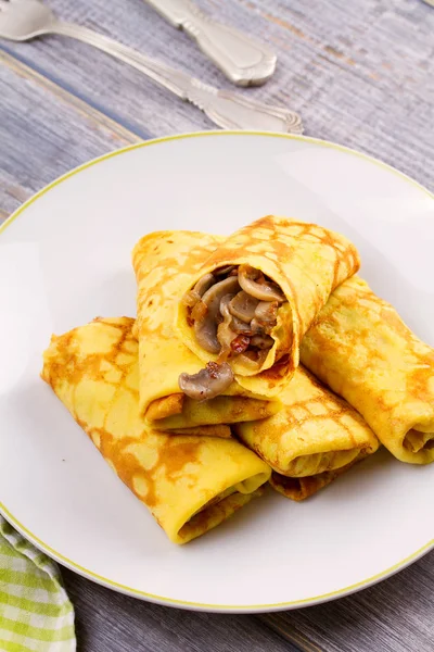 Radbruten tunna pannkakor fyllda med svamp på vit platta — Stockfoto