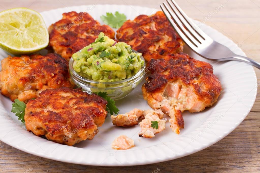 Salmon patties or cakes, lime and avocado on white plate. Fritters of fish. Salmon burgers