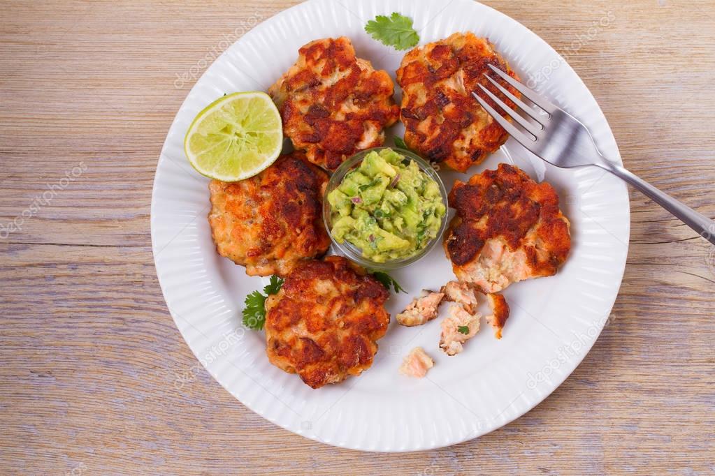Salmon patties or cakes, lime and avocado on white plate. Fritters of fish. Salmon burgers