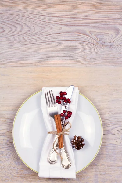 Christmas set with plate, cutlery, pine branches, cinnamon and red berries on wooden place. Winter holidays and festive background. Christmas eve dinner, New Year food lunch