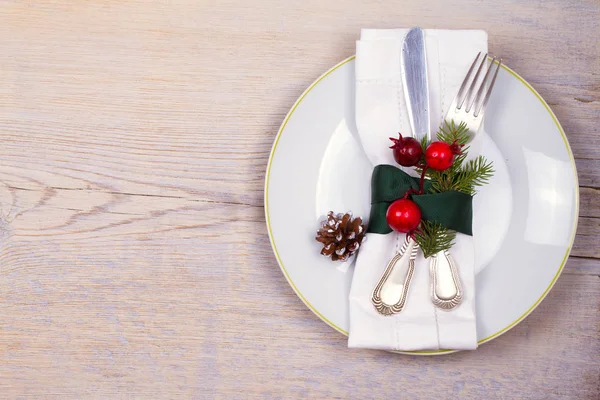 Conjunto de Natal com prato, talheres, ramos de pinho, canela e bagas vermelhas no lugar de madeira. Férias de inverno e fundo festivo. Jantar de véspera de Natal, almoço de comida de Ano Novo — Fotografia de Stock