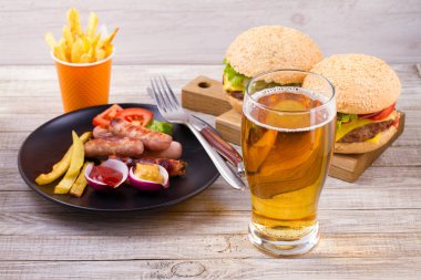 Bardak bira sosis plaka, burgers ve fries ahşap arka plan ile. Bira ve gıda kavramı. Ale ve gıda, yatay