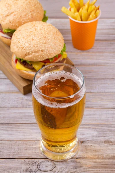 Glass of beer with burger and fries on wooden background. Beer and food concept. Ale and food. vertical