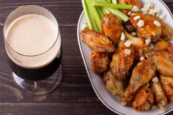 Glass of dark beer and siracha buffalo chicken wings. Ale and food