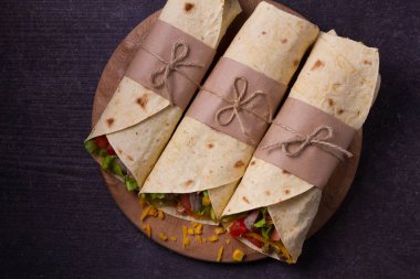 Tortilla, burrito, bükülmüş sandviç rulo. Sığır eti, domates, marul, salatalık, kaşar peynir, Mısır ve soğan halkaları sarar. Yukarıdan görüntülemek, top, yatay