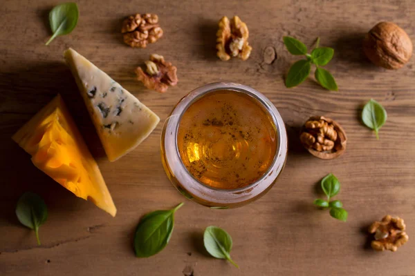 Beer and cheese. Glass of beer with cheese, walnuts and basil on wooden background. Ale and food concept. View from above, top