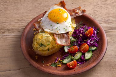 Ceketli fırında patates peynir ile yüklenen ve pastırma ile tepesinde ve sebze ile plaka üzerinde yumurta kızarmış. Tepesi ile doldurulmuş patates 